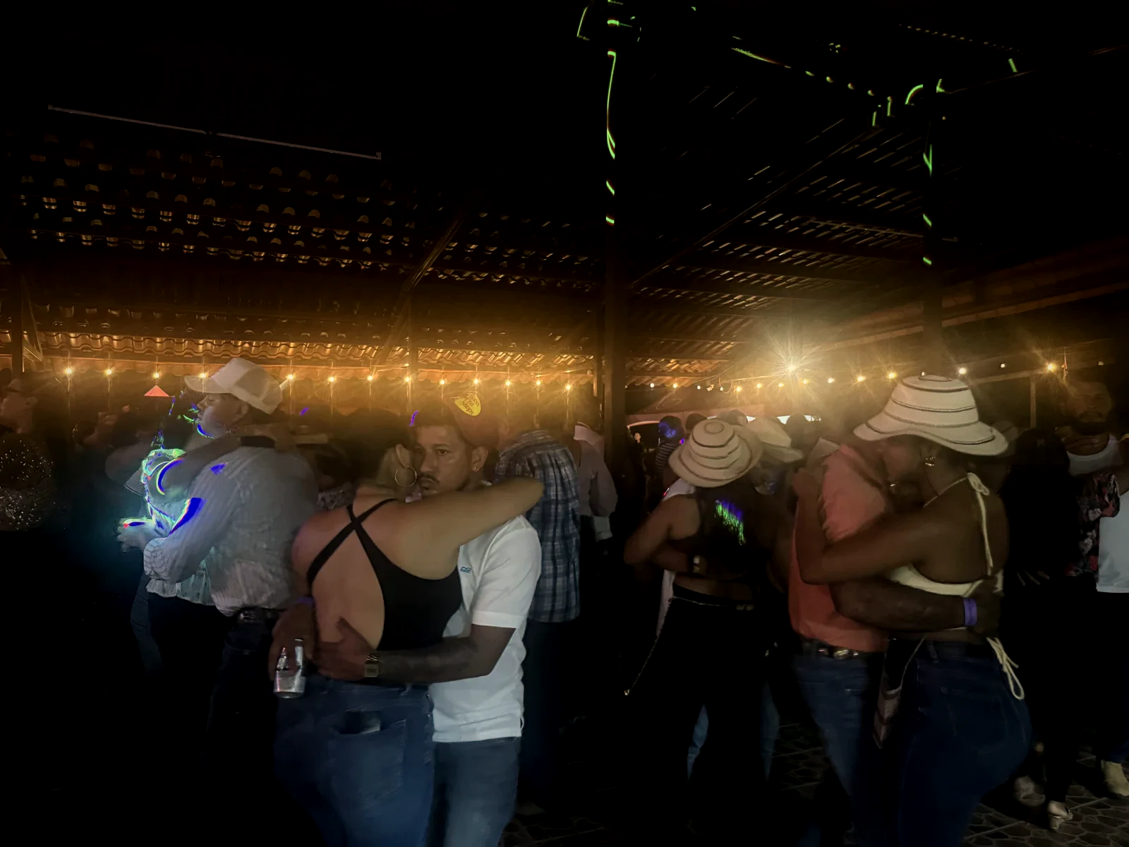 Parejas bailando muy cerca bajo las luces colgantes del rancho, en una noche especial de música en vivo