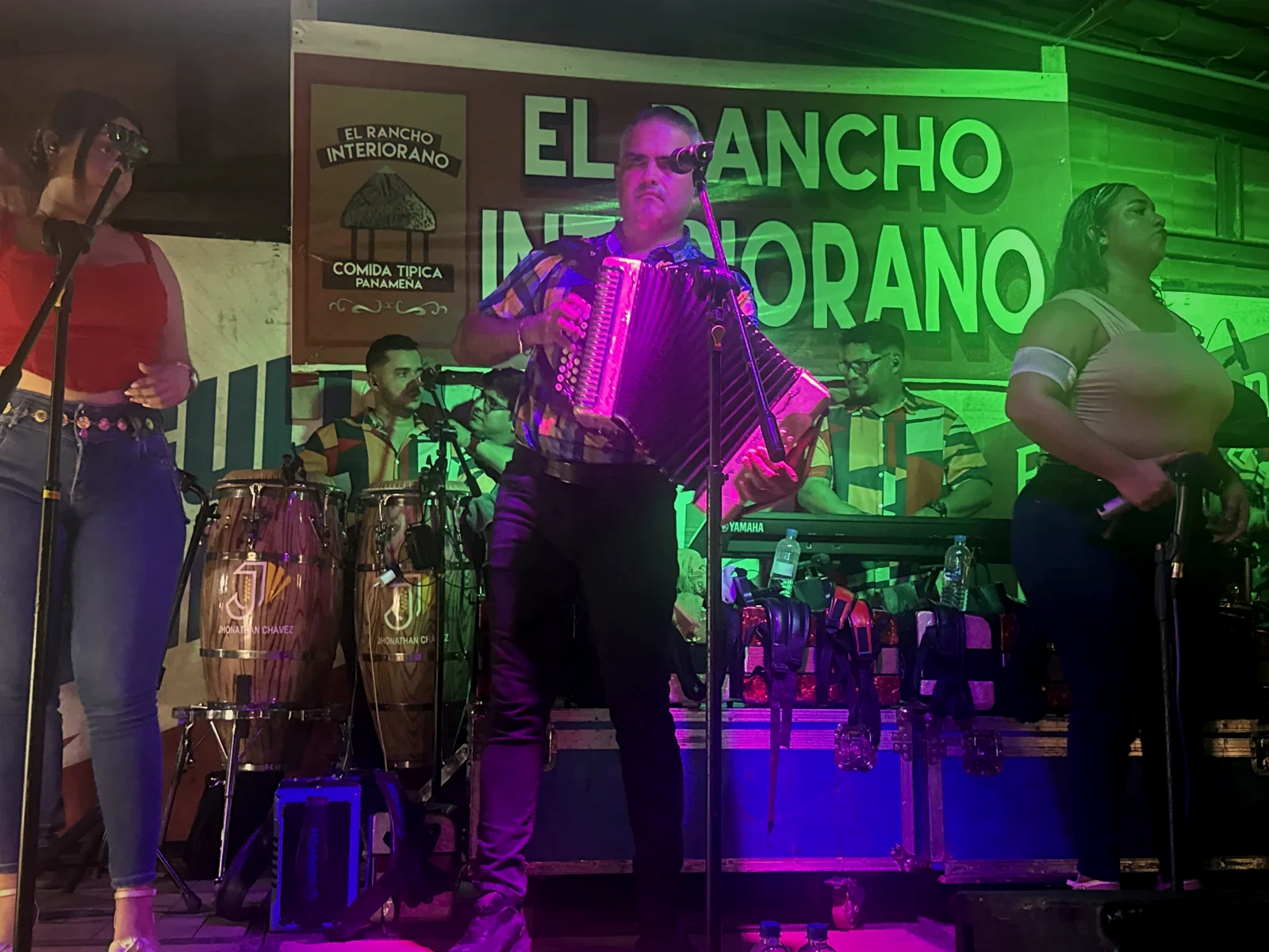 El acordeonista de la orquesta cantando frente al banner de El Rancho Interiorano, con las congas de la tarima al fondo