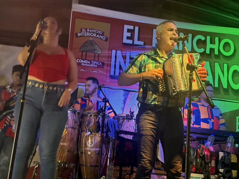 La cantante y el acordeonista de la orquesta en la tarima, con el banner de El Rancho Interiorano — Comida Típica Panameña detrás