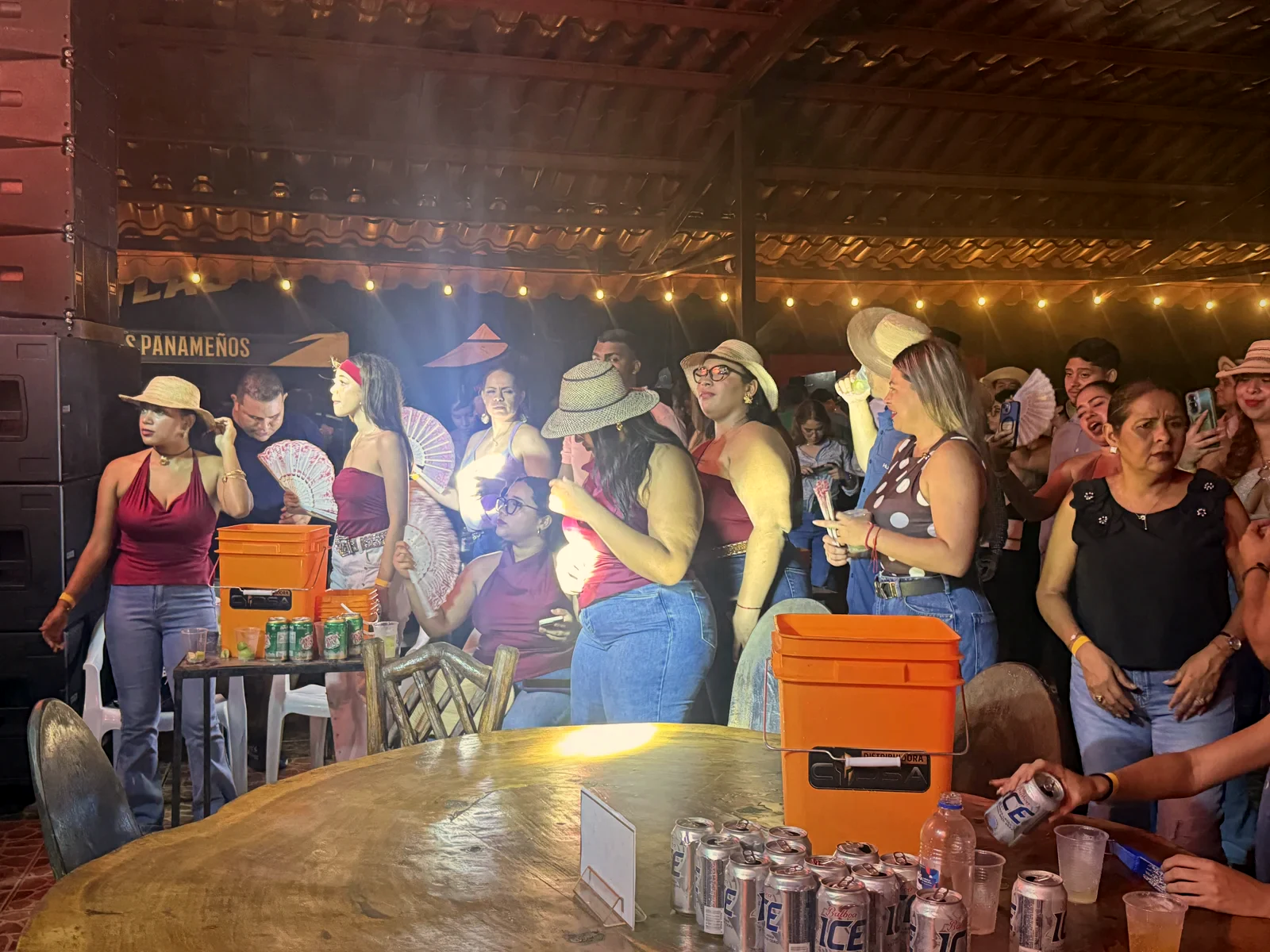Grupo de mujeres con sombreros y abanicos junto a una cava de cervezas, durante una noche especial en el rancho
