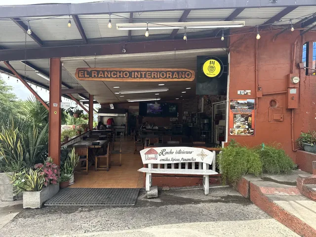 Fachada real de El Rancho Interiorano en su sede de Loma Campana, Capira, con el letrero de madera del restaurante y una banca tallada a la entrada